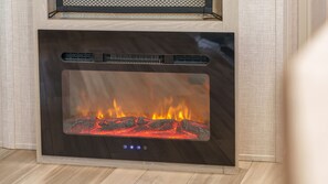 A modern fireplace with a glass front, displaying a fire inside. - Sokcho Supuro Caravan (Sokcho)