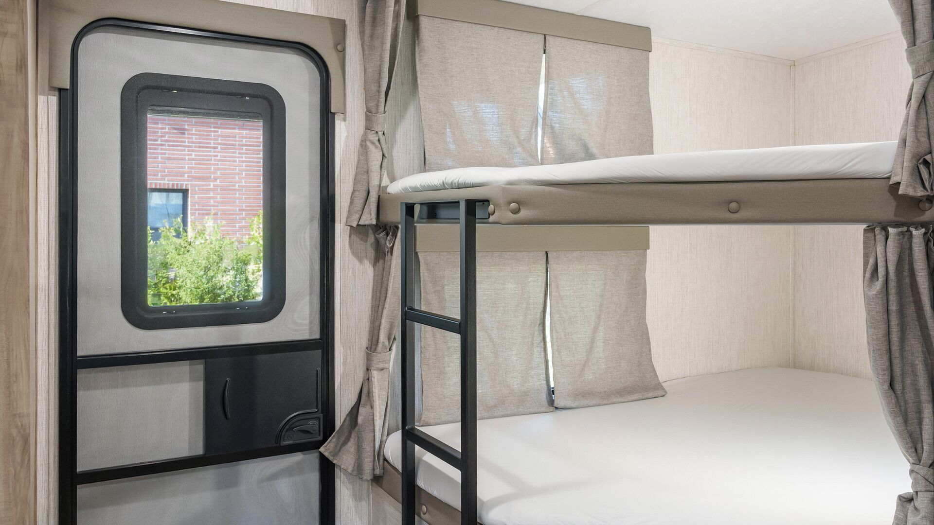 A bunk bed with a window, curtains, and a view of greenery outside.
