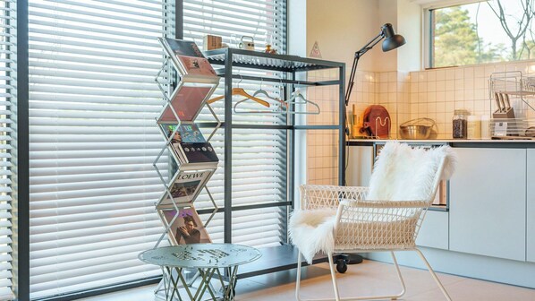 A modern kitchen with a metal rack holding magazines, a white chair, and a small round table. - Sokcho Supuro Caravan (Sokcho)