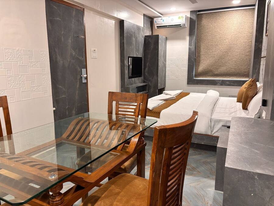 Ein modernes Hotelzimmer mit einem Glastisch, Holzstühlen, einer Couch und einem Fernseher.