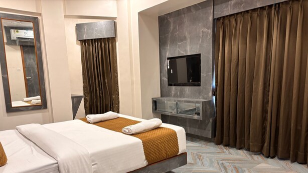 Une chambre d’hôtel moderne équipée d’un lit, d’un téléviseur à écran plat, d’une coiffeuse et d’une grande fenêtre avec des rideaux.
