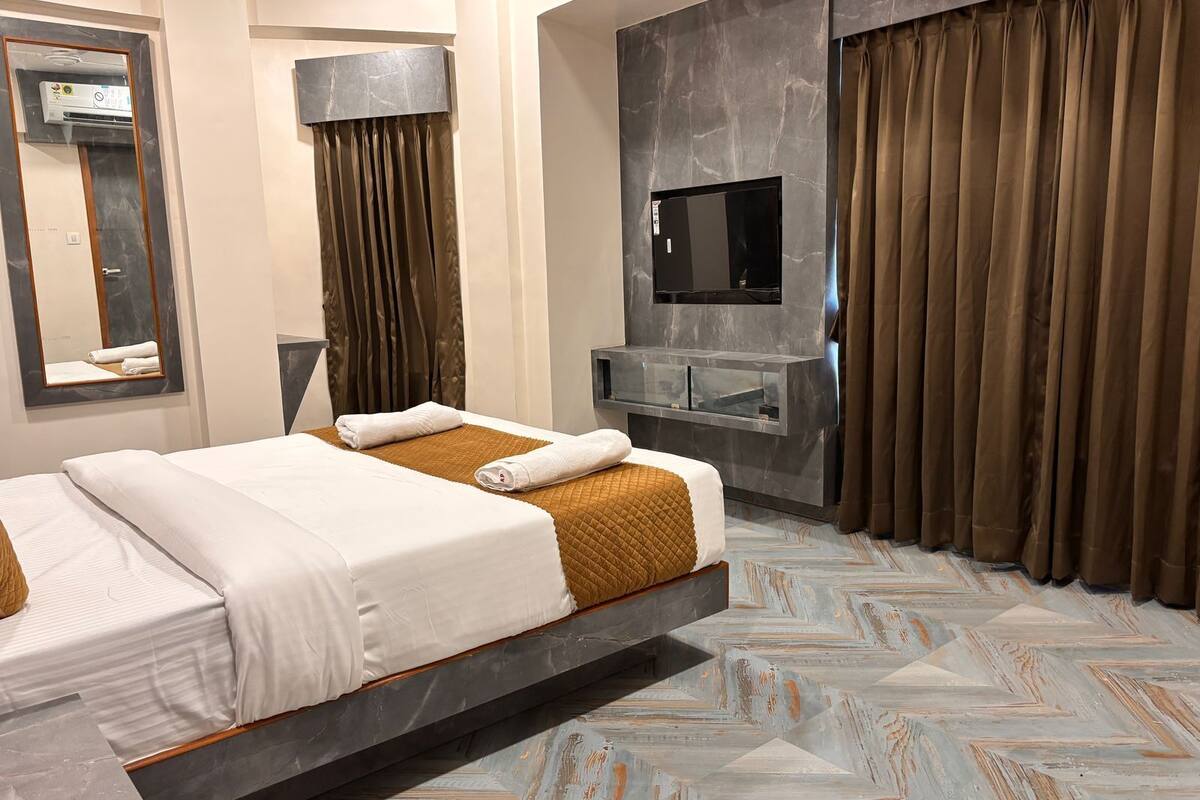 Een moderne hotelkamer met een bed, een flatscreen televisie, een kaptafel en een groot raam met gordijnen.