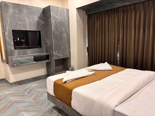 A hotel room with a bed, a flat-screen TV mounted on a stone wall, a small shelf, and a window with curtains. - HOTEL ARTS PALACE (Mumbai)