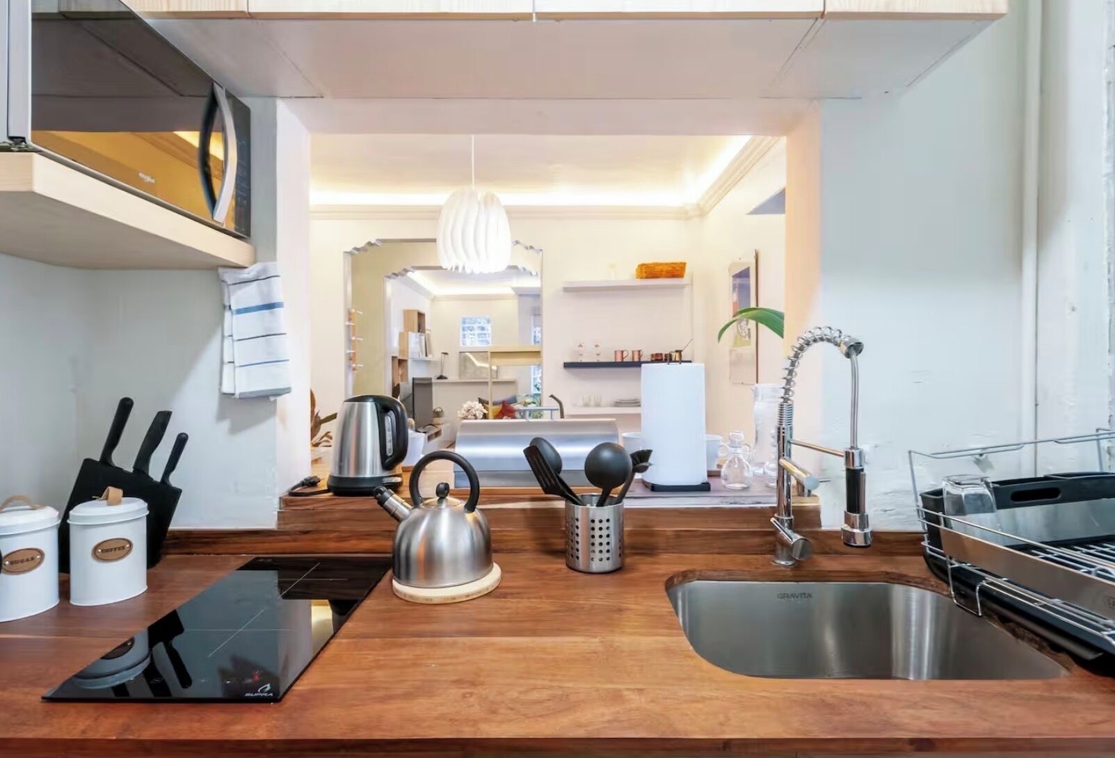 Une cuisine moderne avec un plan de travail en bois, une bouilloire, un support pour bouilloire, une autre bouilloire, une machine à café, un évier et une bouilloire sur la cuisinière.