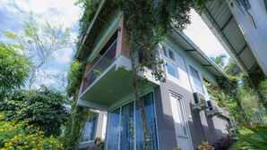 A multi-story building with balconies, large windows, and lush greenery. - Floresta resorts (Idukki)