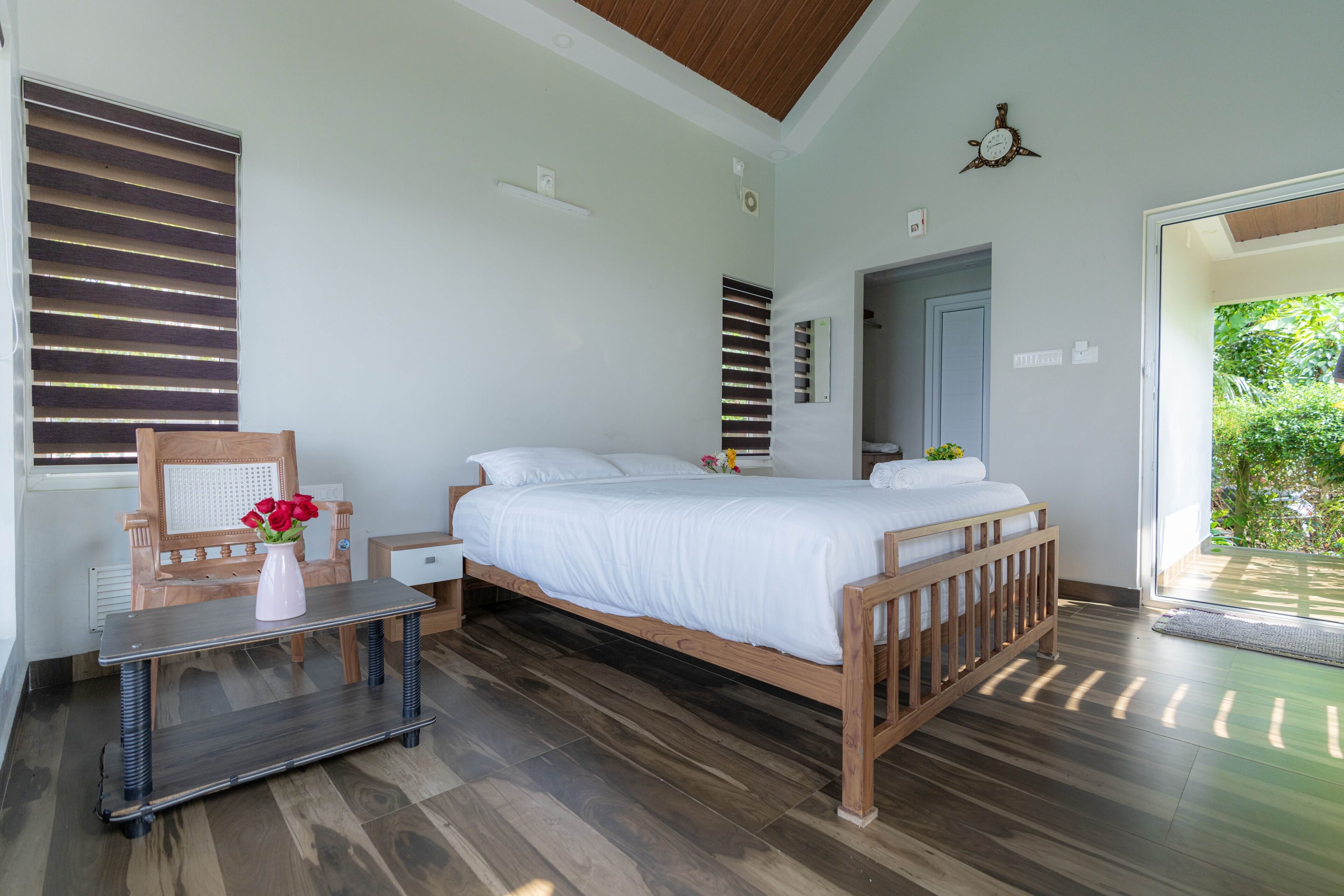 A bedroom with a wooden bed, a bedside table, a chair, and a window with blinds.