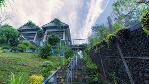 A staircase leading up to a building with a traditional architectural style, surrounded by lush greenery and a cloudy sky. - Floresta resorts (Idukki)
