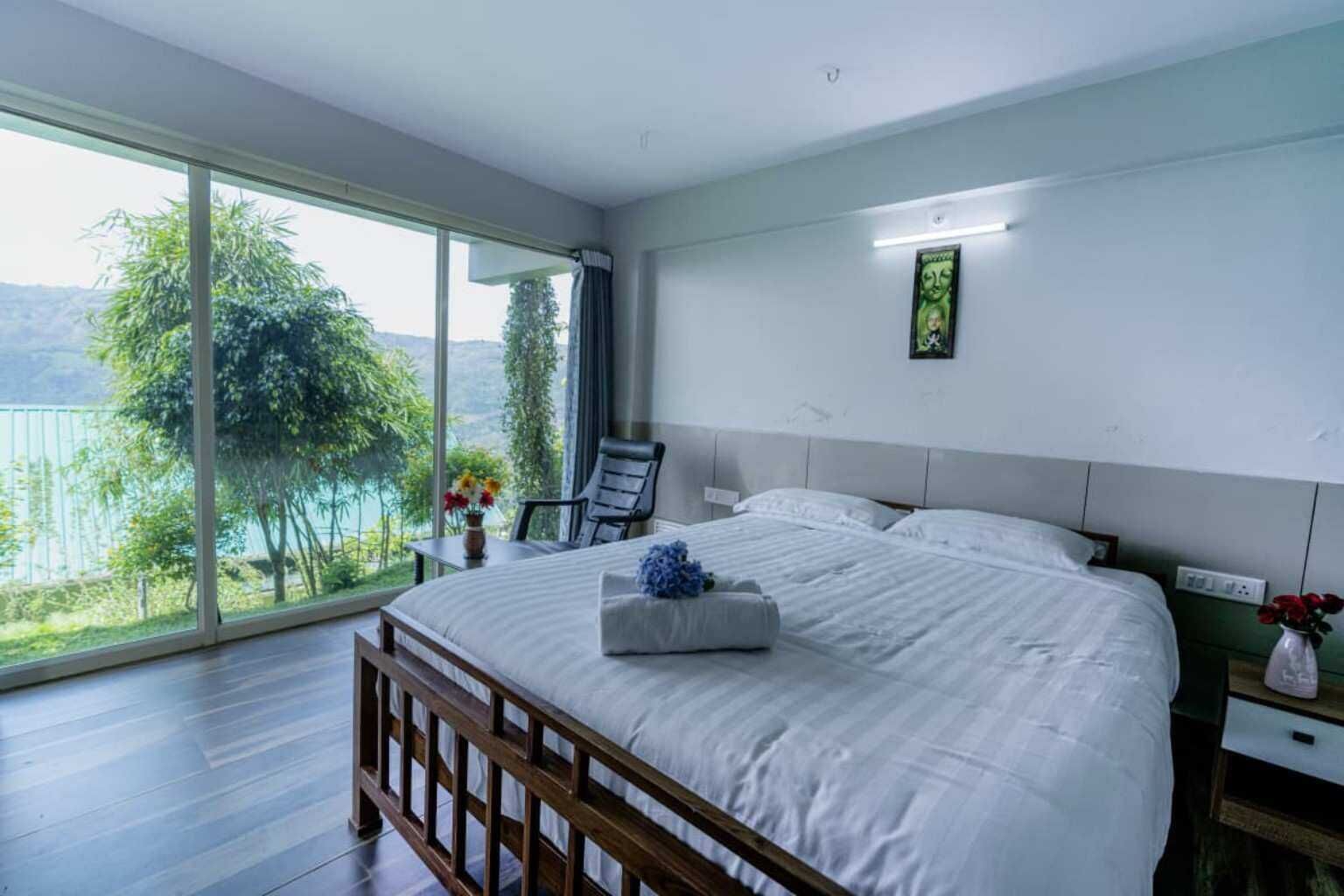 Ein Schlafzimmer mit einem großen Bett, einem Sessel, einem Nachttisch und Blick auf einen See.