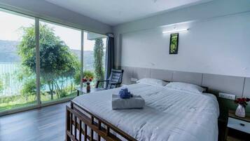 Ein Schlafzimmer mit einem großen Bett, einem Sessel, einem Nachttisch und Blick auf einen See.
