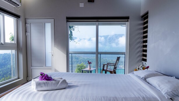 A bedroom with a large bed, a view of mountains through a sliding door, and a balcony with a chair and flowers. - Floresta resorts (Idukki)