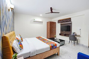 A hotel room with a bed, a desk, a chair, a TV, and a ceiling fan. - Fabhotel Divine & Banquet (Noida)