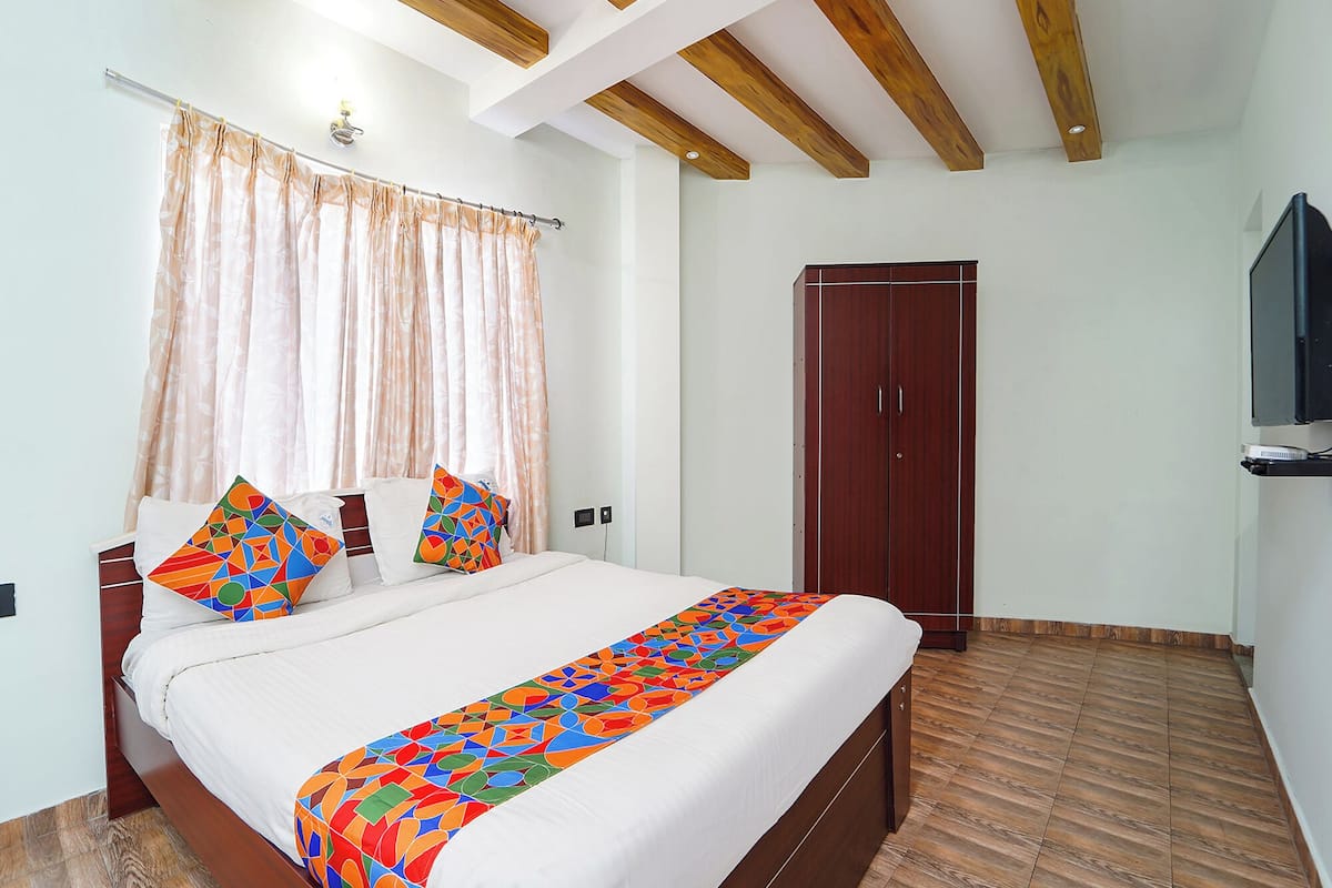 Un dormitorio con una cama, un armario de madera, un televisor y una ventana con cortinas.