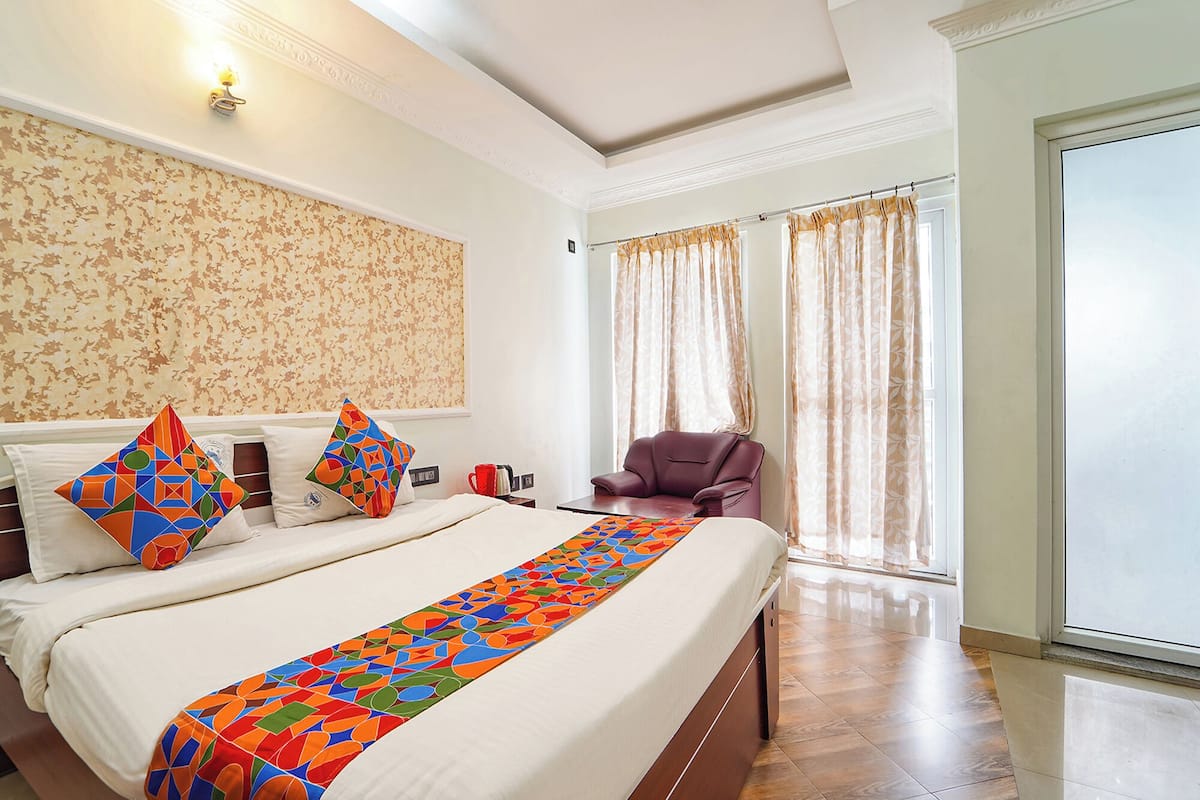 Una habitación de hotel con una cama grande, una silla, un escritorio y un ventanal con cortinas.