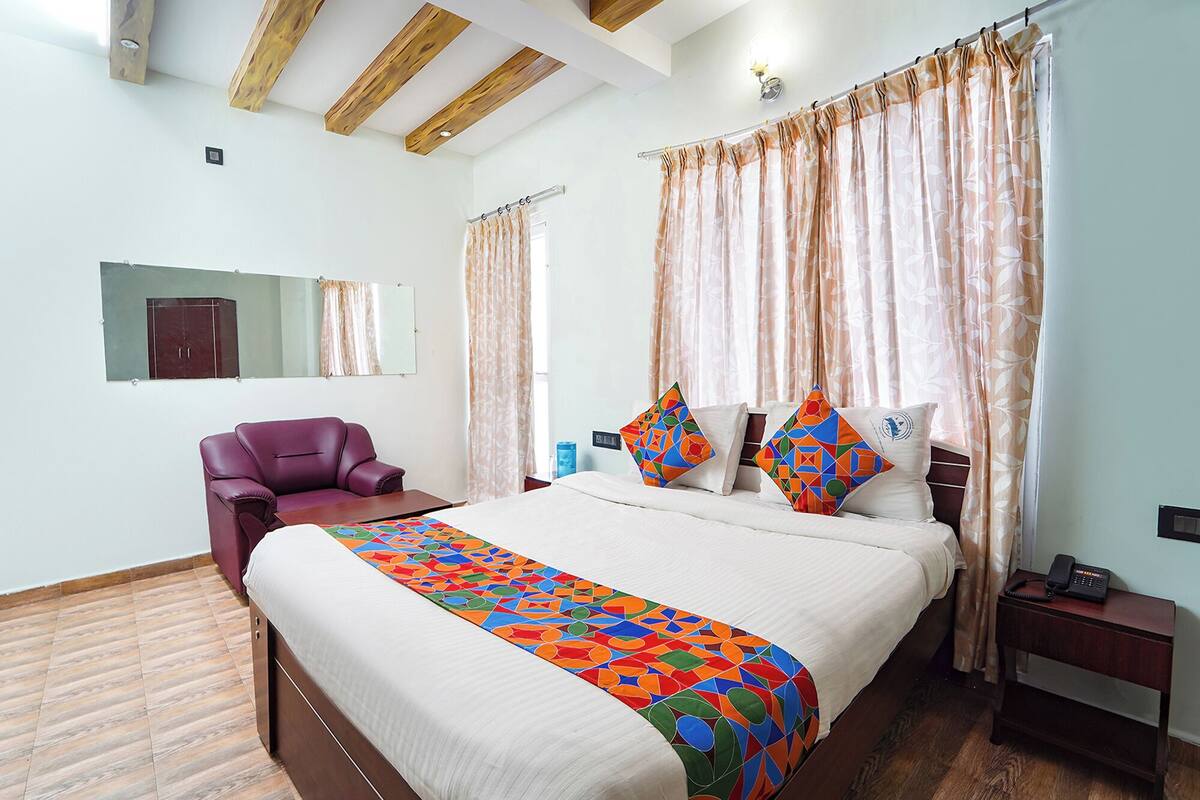 Una habitación de hotel con una cama, una silla, una mesita de noche, un espejo y cortinas.