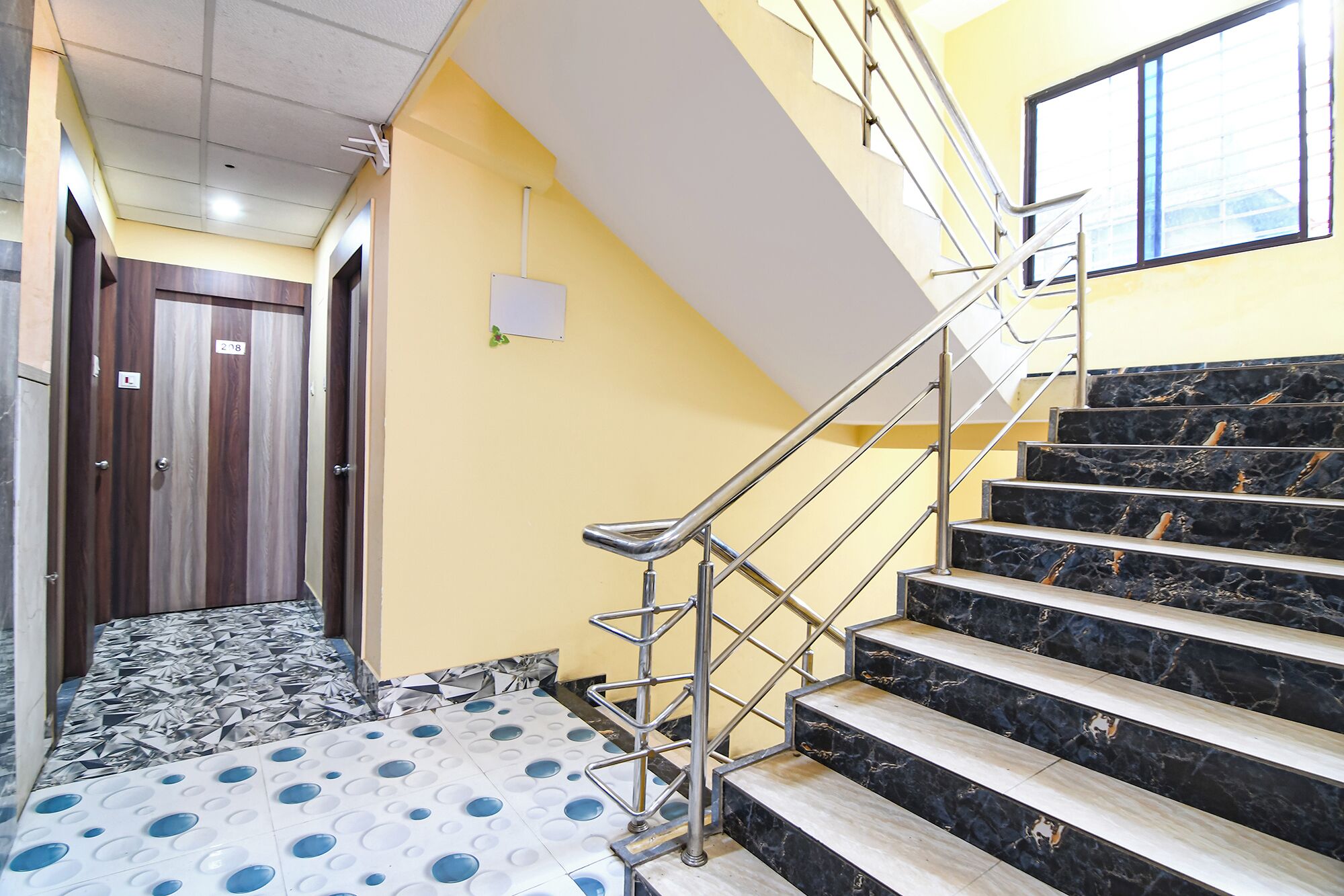 A staircase with black and white marble steps, a metal handrail, and a yellow wall with a whiteboard.