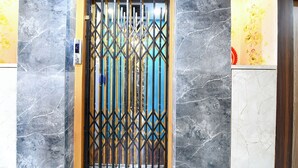 Ein moderner Aufzug mit einem geometrischen Metallgitter, Marmorwänden und einer gelben Akzentwand.