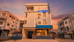 Un edificio moderno de varios pisos con un letrero 'fabHOTELS', que presenta una fachada plana, varios balcones y una entrada a nivel de calle con un pequeño área de estar al aire libre.