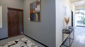 Un pasillo con una puerta de madera, un cuadro en la pared, una consola con un jarrón y una alfombra estampada.