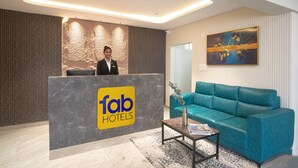 Un mostrador de recepción con un logotipo, una recepcionista, un sofá color turquesa y un cuadro en la pared.