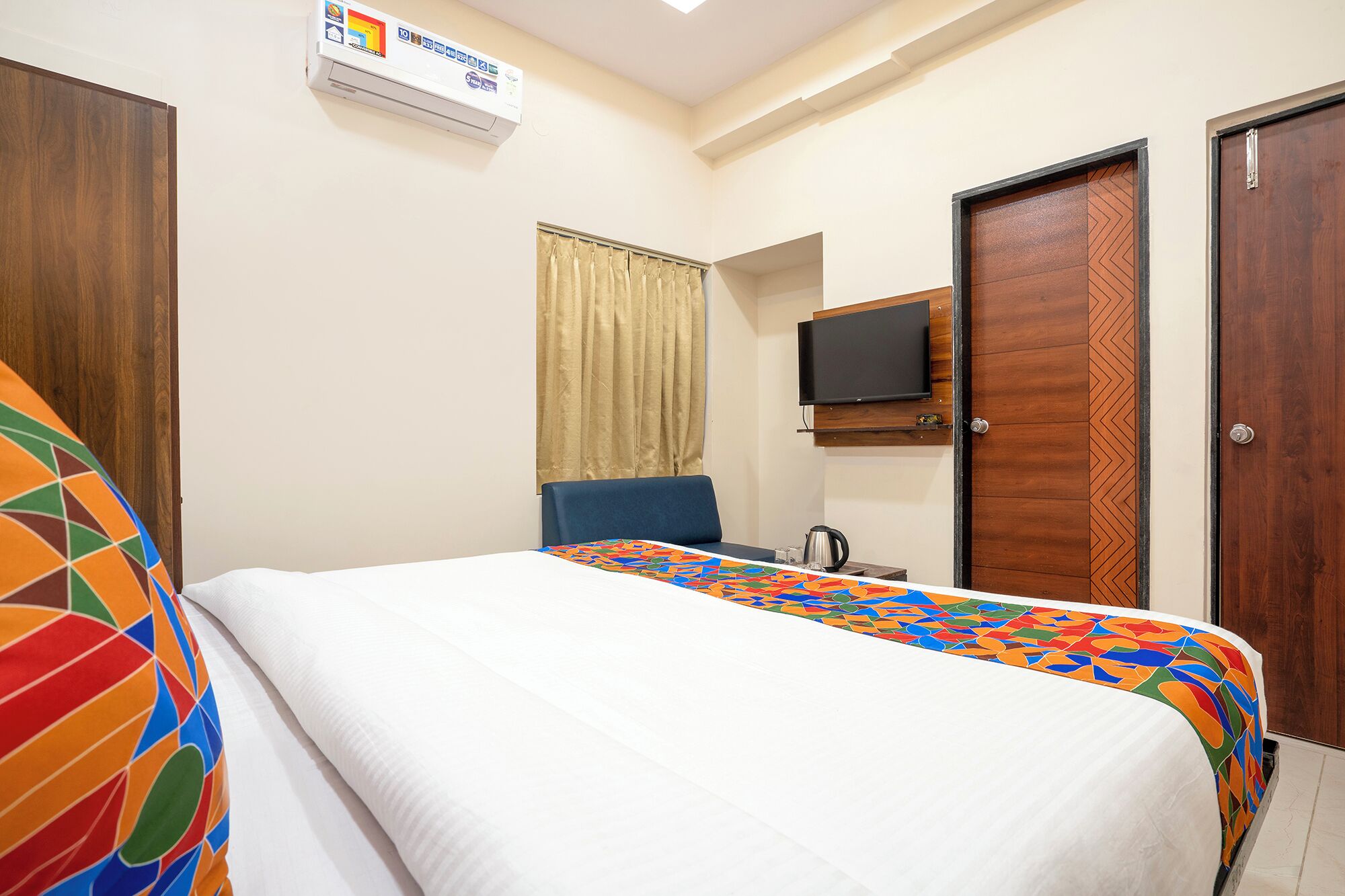 A hotel room with a bed, a television, and a window with curtains.