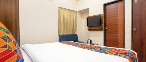 A hotel room with a bed, a television, and a window with curtains.