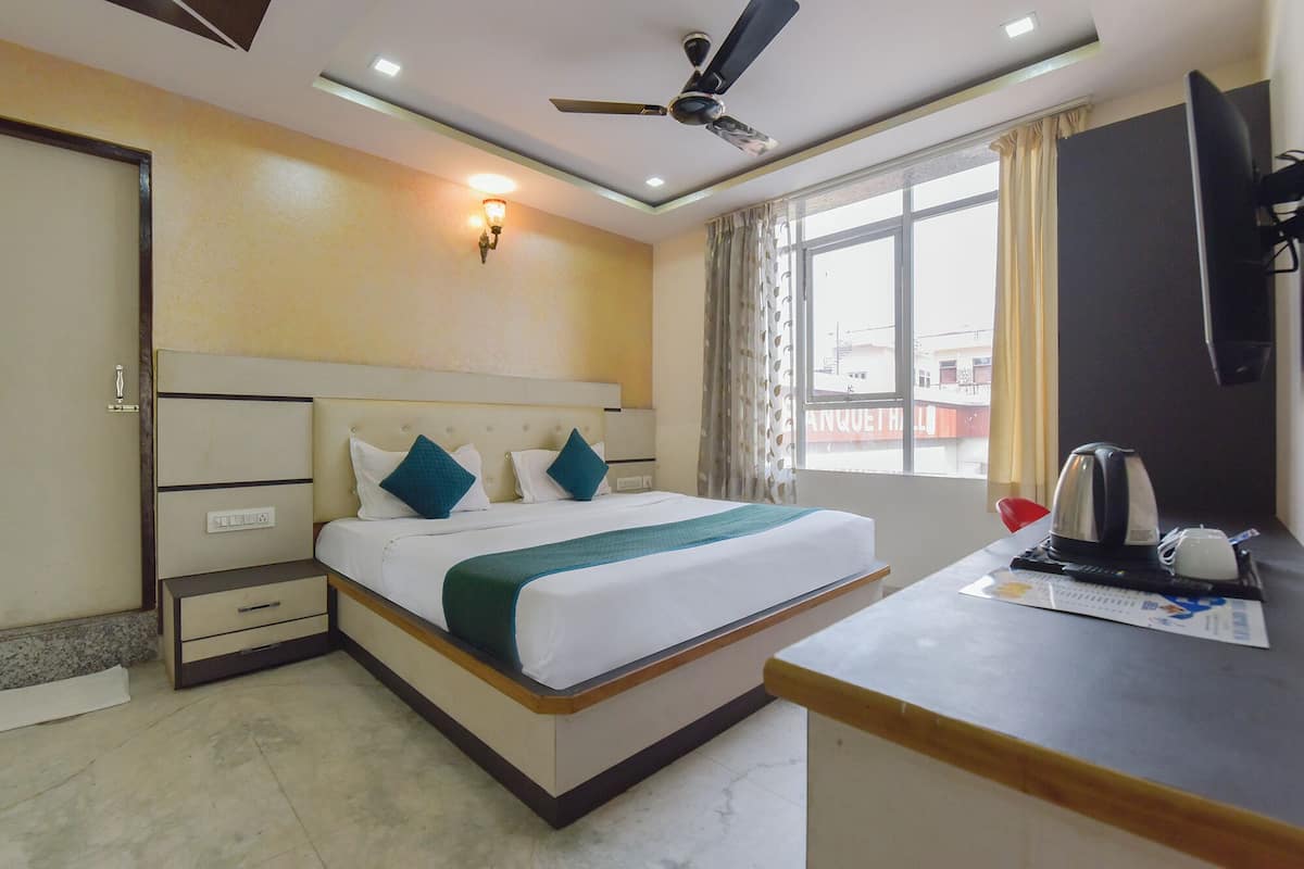 Une chambre d’hôtel avec un lit, une table de chevet, un ventilateur de plafond, une fenêtre avec des rideaux et un téléviseur fixé au mur.