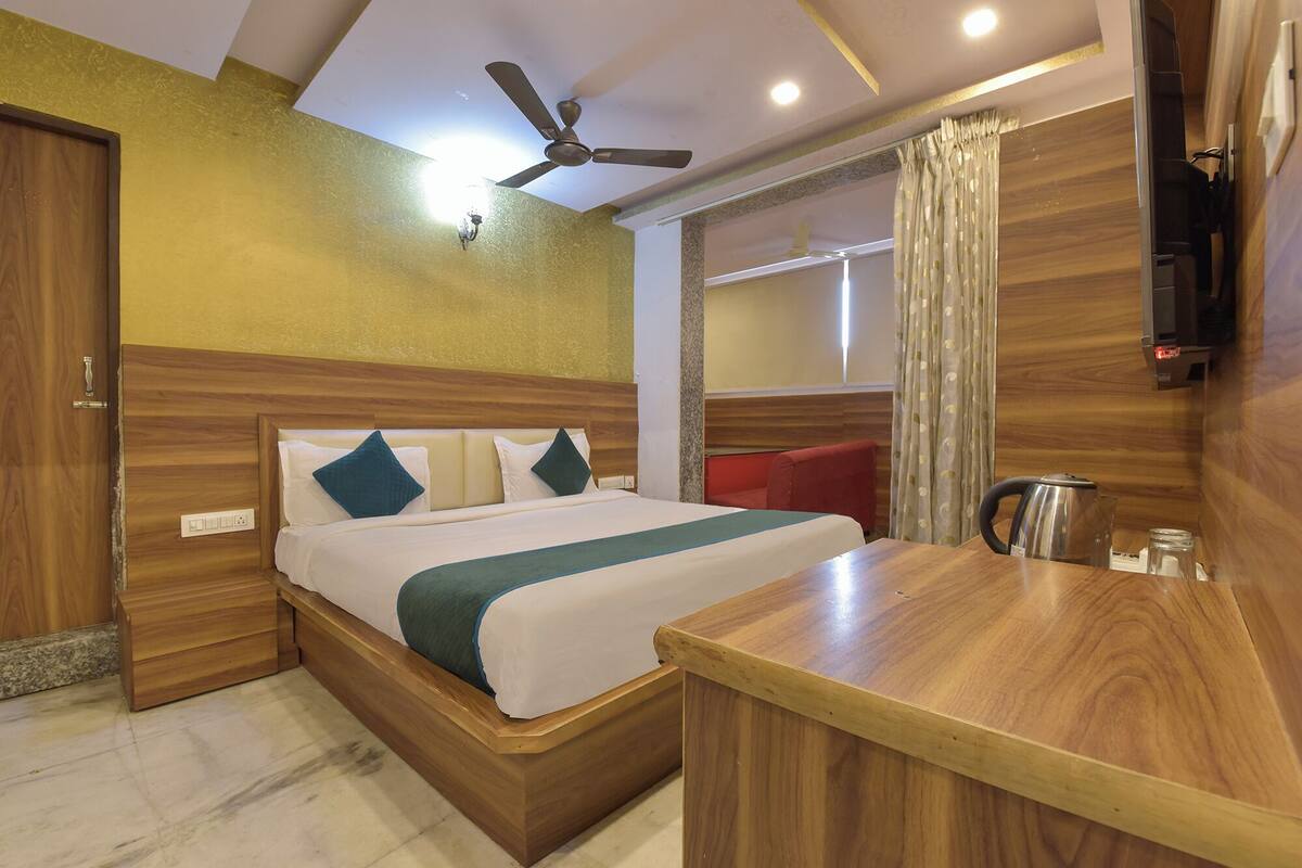 Une chambre d’hôtel avec un lit en bois, un bureau, un ventilateur de plafond et un téléviseur fixé au mur.