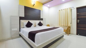 A modern hotel room with a large bed, a bedside table, a nightstand, a wall-mounted light fixture, and a door with curtains. - Fabhotel Prime Airport View (Jaipur)