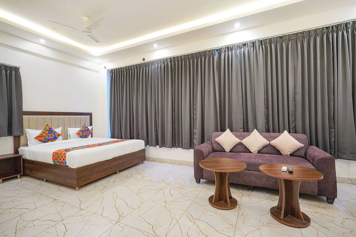 A hotel room with a bed, a sofa, two side tables, and a ceiling fan.