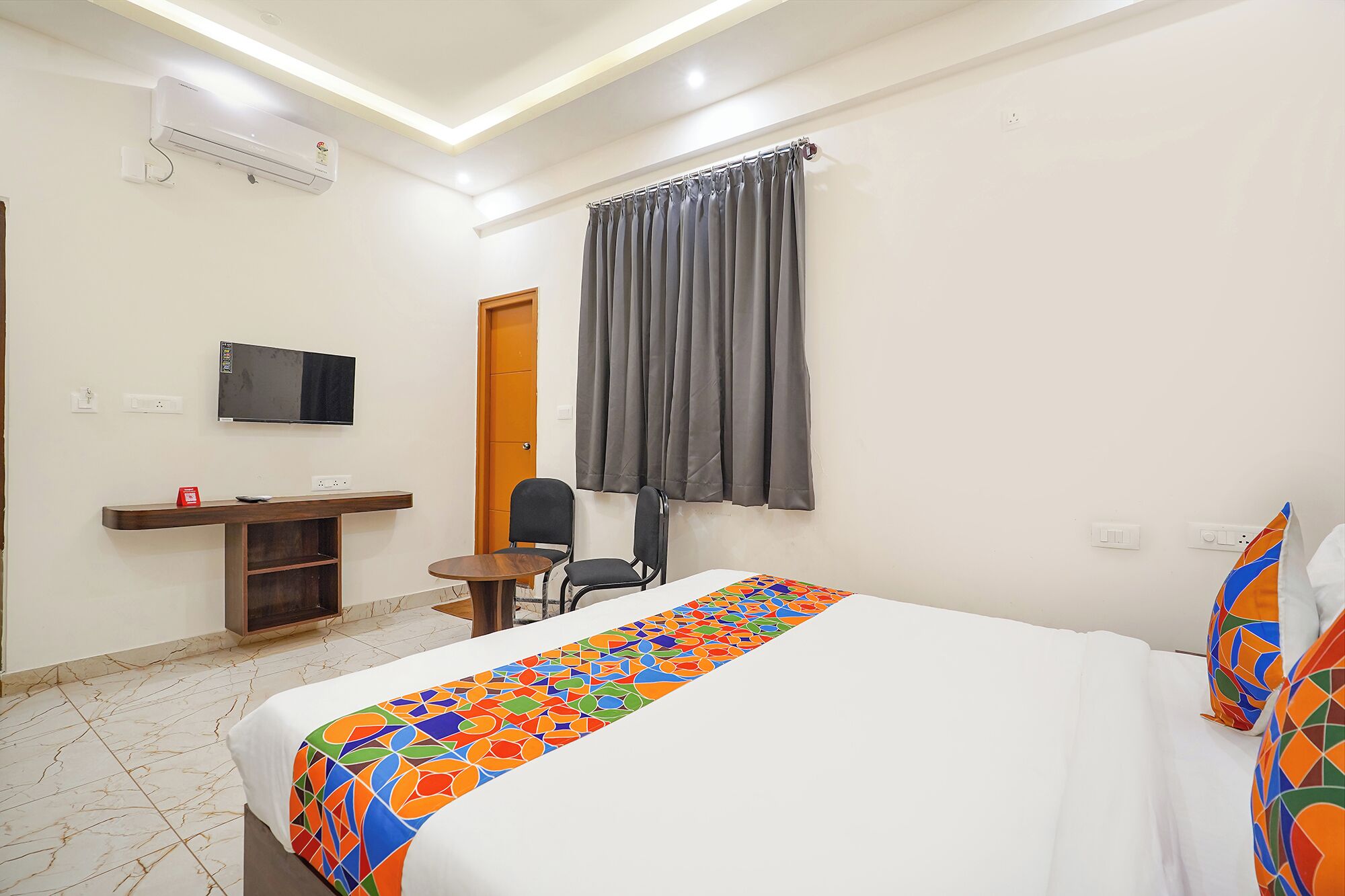 Habitación de hotel con cama, escritorio con silla, televisor y ventana con cortinas.