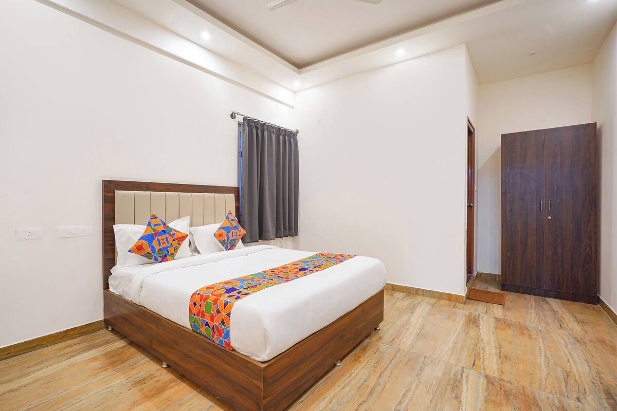 A hotel room with a wooden bed, a grey curtain, a wooden wardrobe, and a tiled floor.