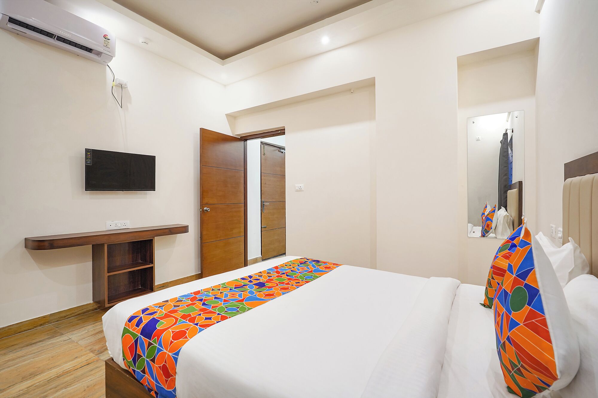 A hotel room with a bed, a TV, a wooden wardrobe, and a mirror.