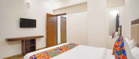 A hotel room with a bed, a TV, a wooden wardrobe, and a mirror.