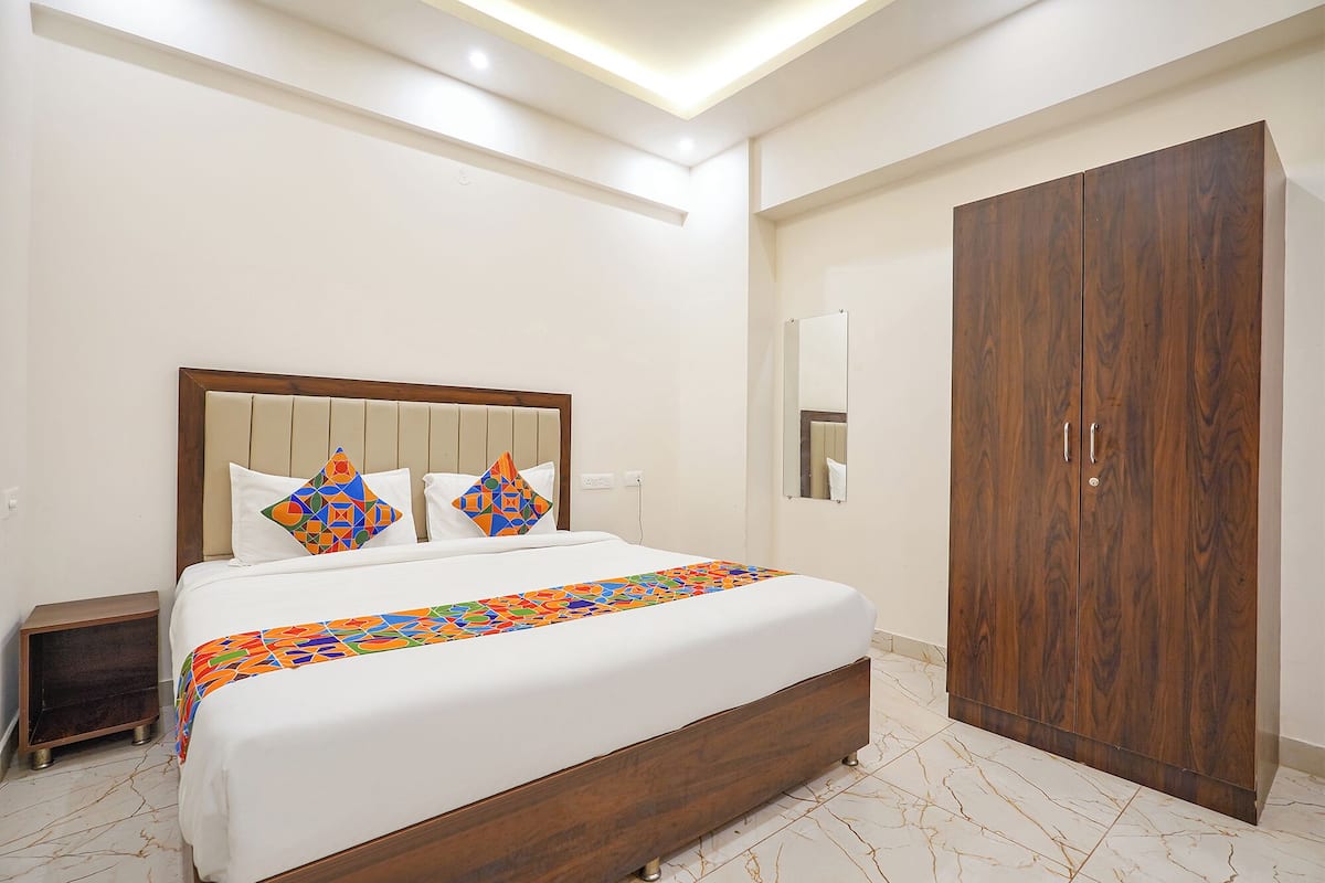 A hotel room with a large bed, a wooden wardrobe, a nightstand, and a mirror on the wall.