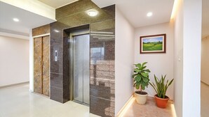A modern elevator with marble walls, a potted plant, and a framed landscape picture in a hallway. - FabHotel Indian Suites - Krishnarajapuram (Bangalore)