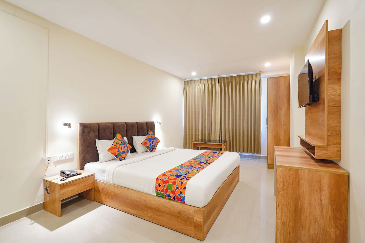 A hotel room with a bed, a bedside table with a phone and charger, a TV mounted on the wall, and a curtain.