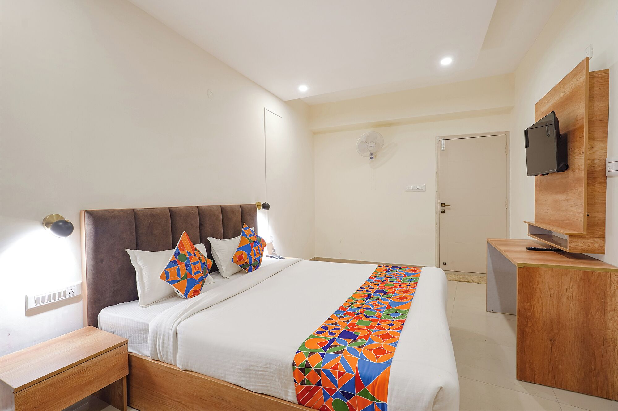 A hotel room with a bed, bedside table, TV, and a wooden cabinet.