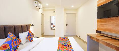 A hotel room with a bed, a TV mounted on the wall, and a hallway leading to a door.