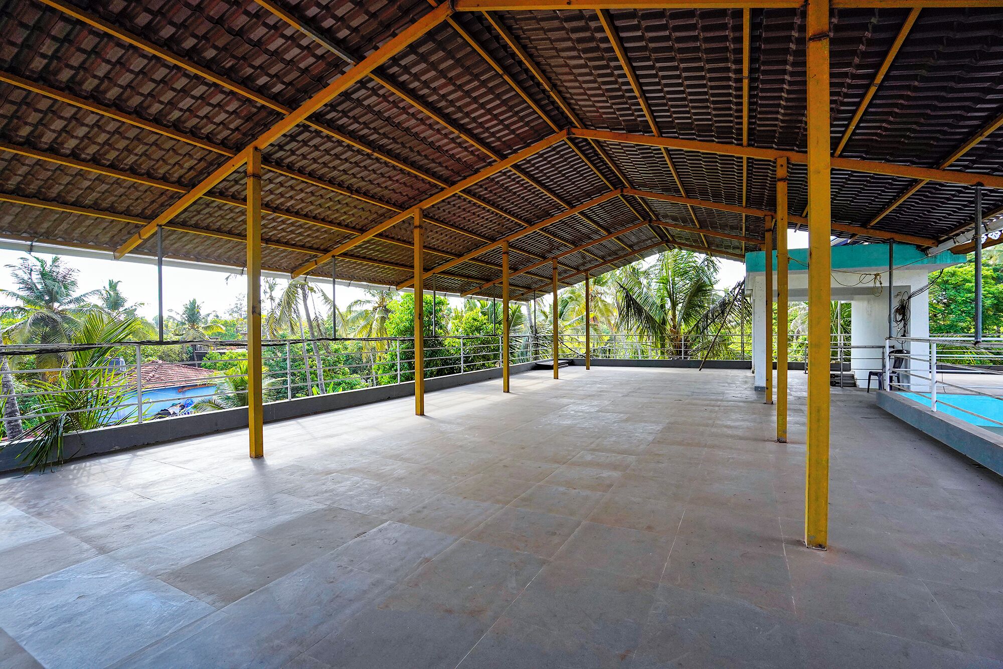 An open covered area with a tiled floor, metal railings, and a view of a swimming pool and greenery.