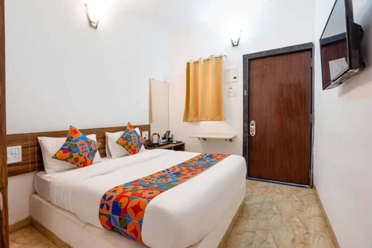 Ein Hotelzimmer mit einem Bett, einem Holz-Kopfteil, einem an der Wand befestigten Fernseher, einer Tür und einem mit Vorhängen ausgestatteten Fenster.