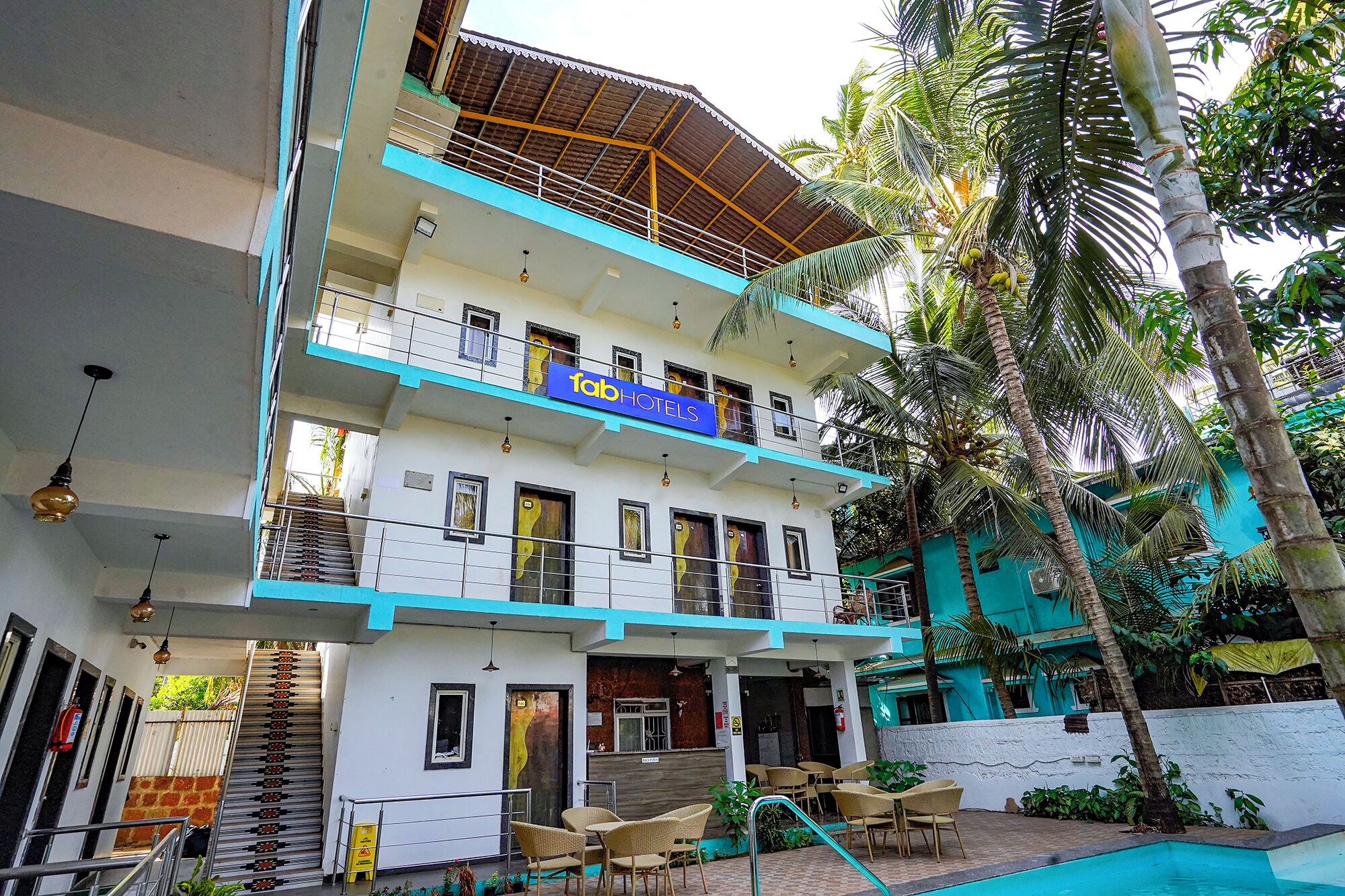 A two-story building with a sign for 'fob hotels'. There are outdoor seating areas and a pool.