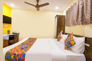 A hotel room with a bed, a desk with a chair, a ceiling fan, and a wardrobe. - Via Metro Galaxy Inn (Mumbai)