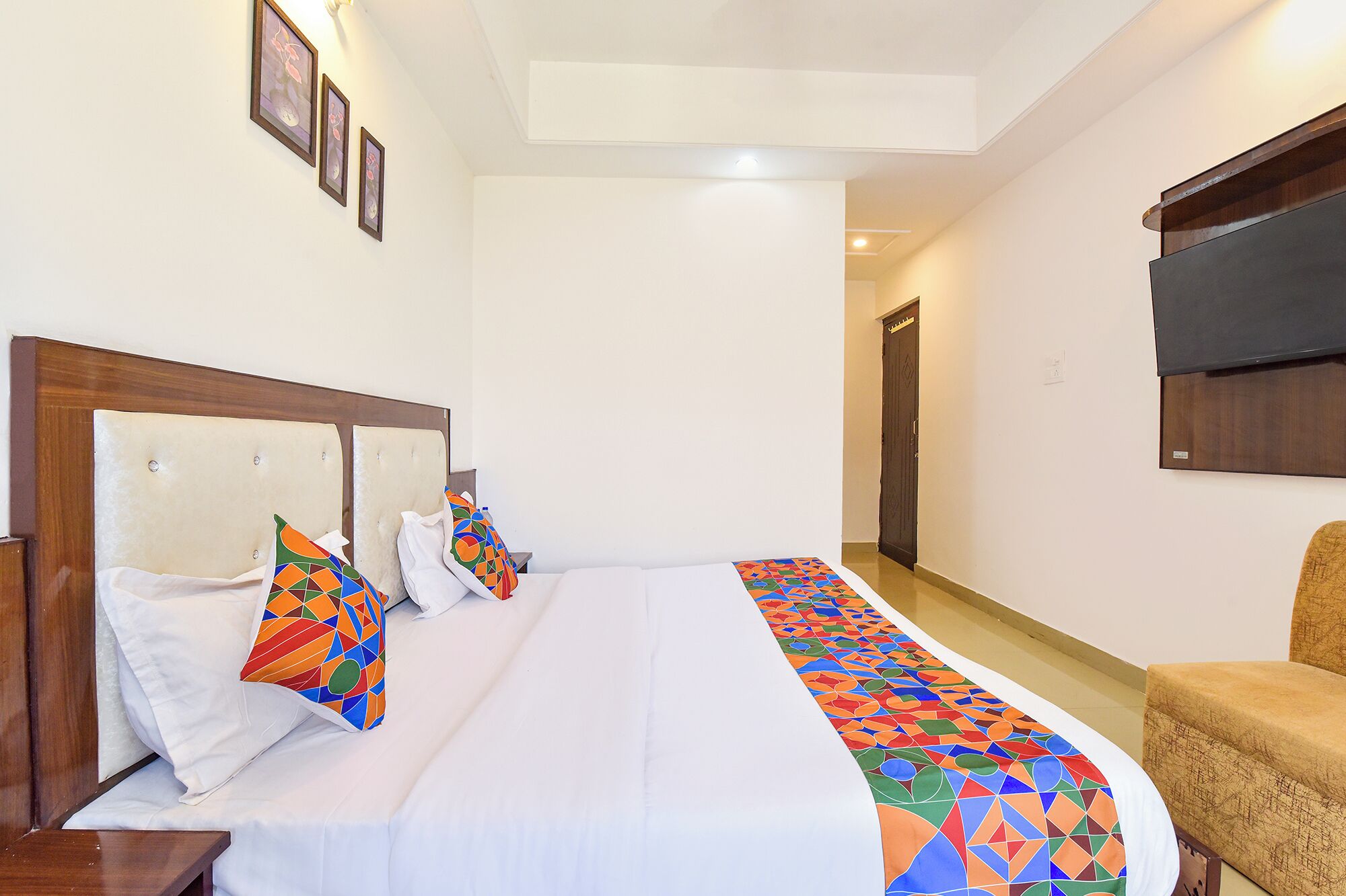 Una habitación de hotel con cama, televisor montado en la pared y una silla.
