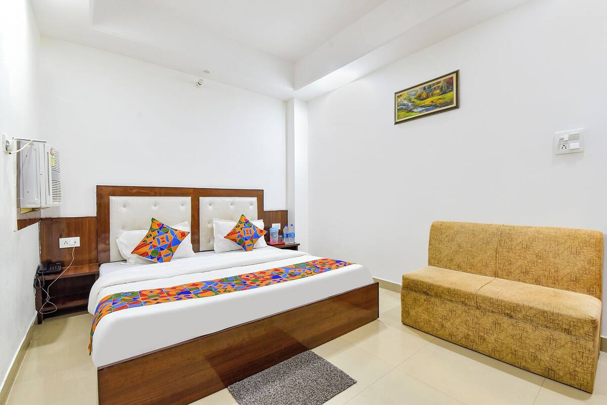 A hotel room with a bed, a sofa, a painting on the wall, and a power outlet.