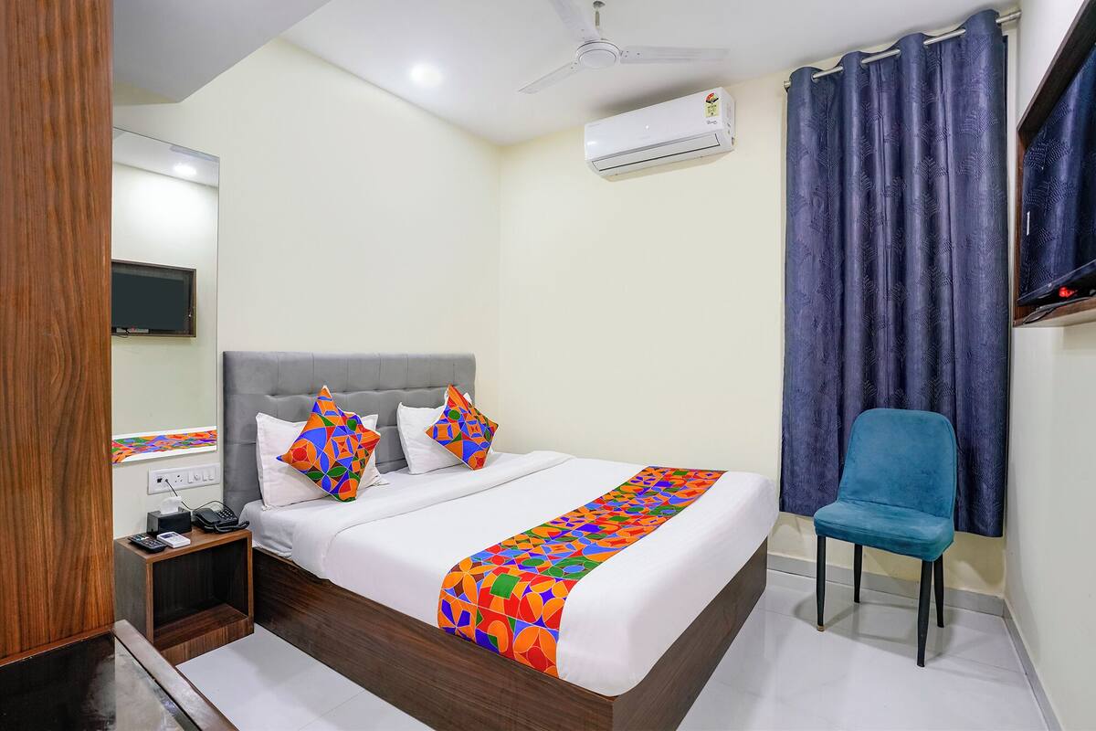 A hotel room with a bed, a desk with a telephone, a chair, a TV, and an air conditioning unit.