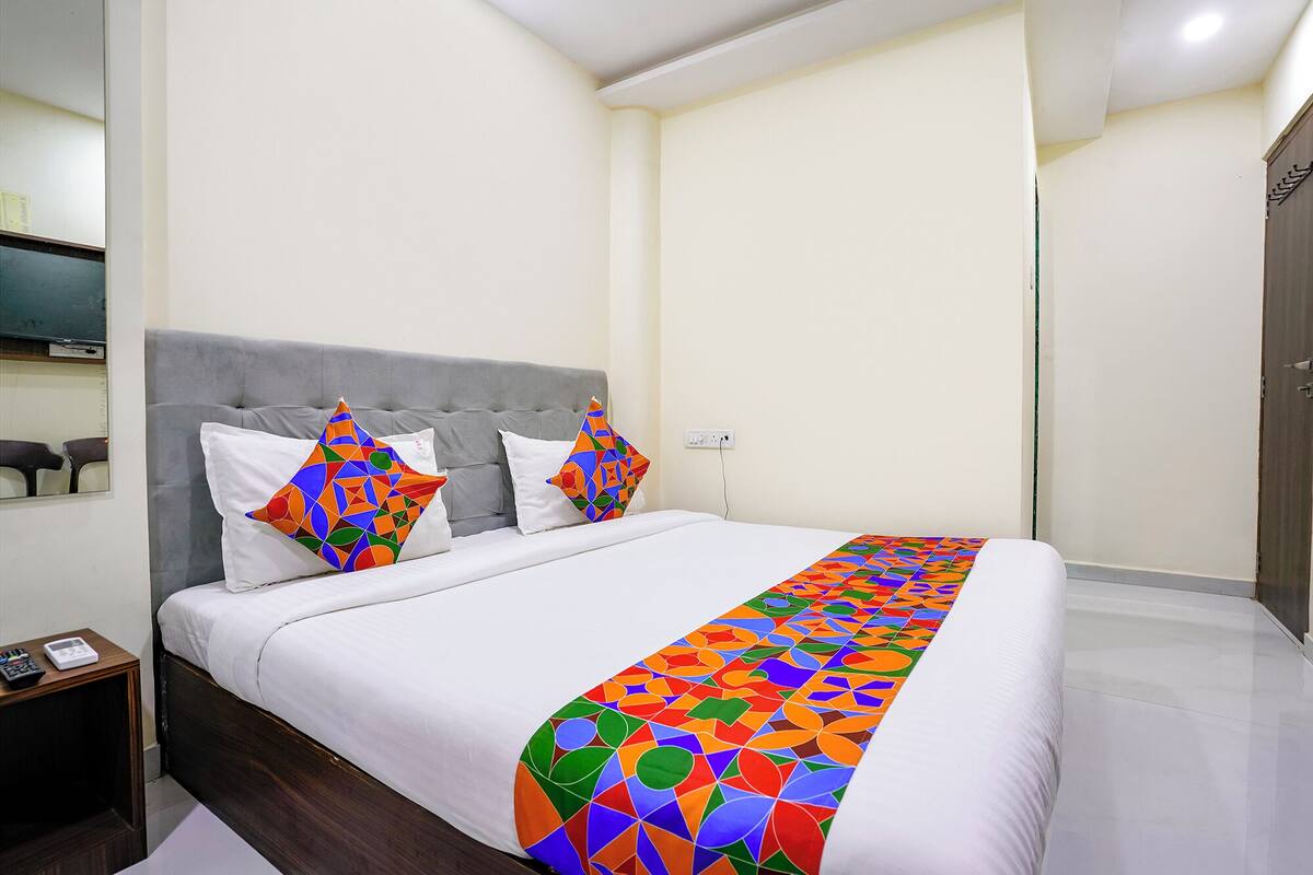 A neatly made bed with a colorful geometric-patterned bedspread, a grey upholstered headboard, and two matching pillows.
