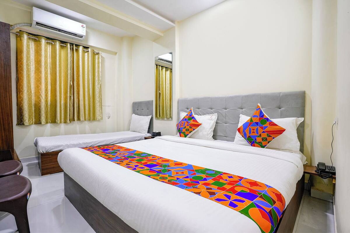 A hotel room with a large bed, two bedside tables, a grey upholstered headboard, and a colorful geometric-patterned bed runner.