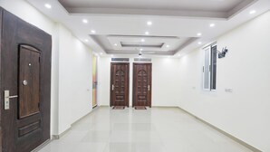 A hallway with two wooden doors, a ceiling with recessed lighting, and a window on the right wall. - Fabhotel Trident (New Delhi)