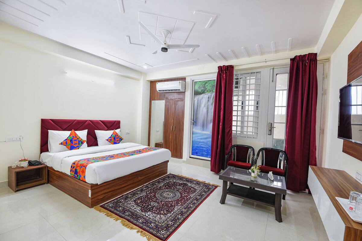 A hotel room with a bed, a desk, a chair, a TV, and a window with curtains.