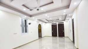 A spacious hallway with a tiled floor, a ceiling fan, recessed lighting, and two dark wooden doors. - Fabhotel Trident (New Delhi)